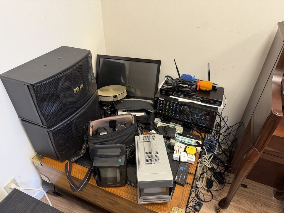 Karaoke speakers, amplifier, monitor and vintage electronics stacked on a wood table at Duluth estate sale